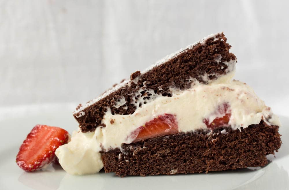 close up slice chocolate cake with strawberries and cream